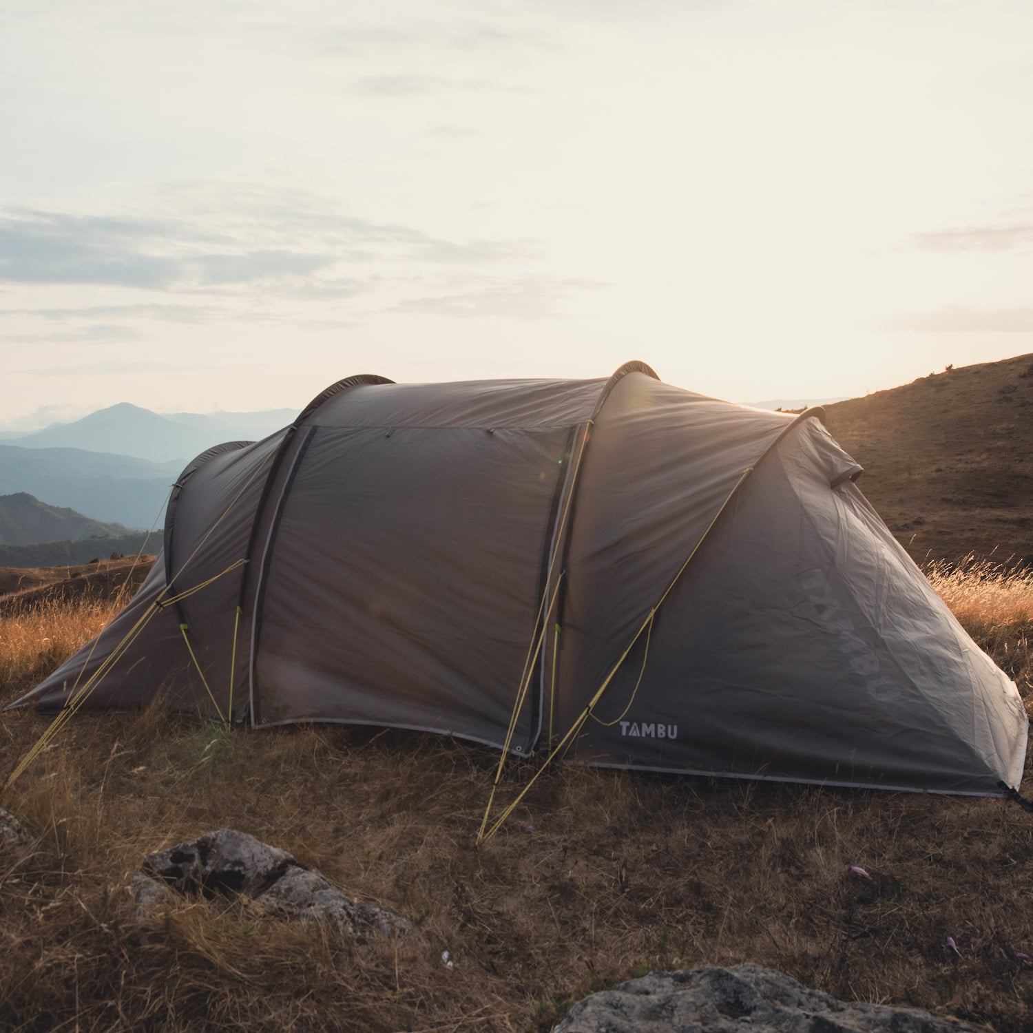 AGNIKUNDA 4-Personen Trekkingzelt von Tambu Outdoor, braun, auf einer Wiese mit Bergen im Hintergrund bei Sonnenuntergang