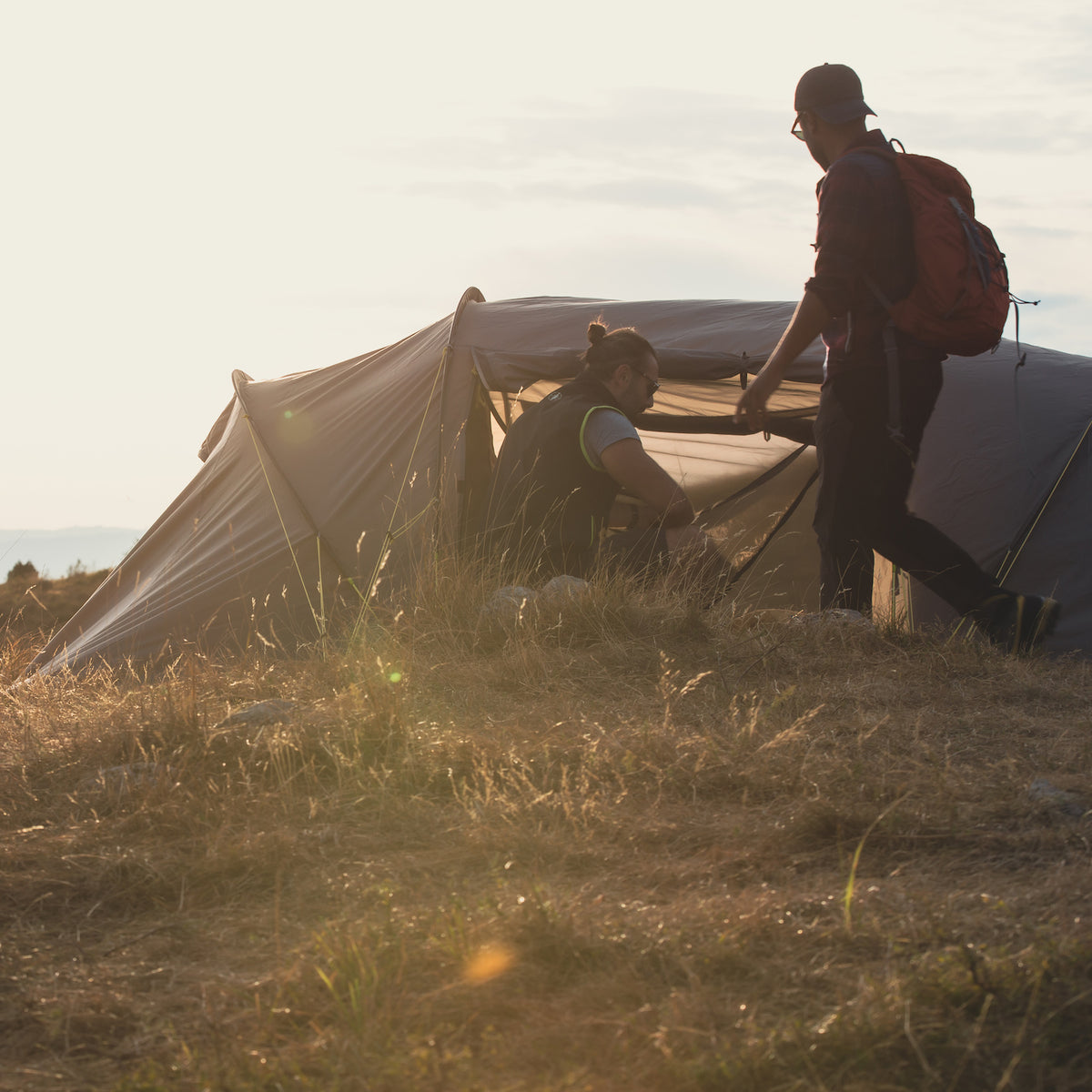 Zwei Personen vor einem AGNIKUNDA 4-Personen Trekking Vis-à-Vis Zelt von Tambu Outdoor auf einer Wiese bei Sonnenuntergang