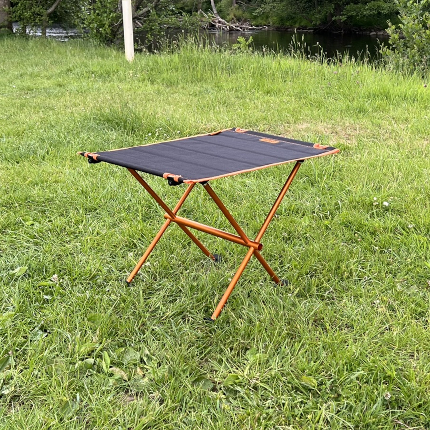 Leichter Campingtisch BATISTA von Tambu Outdoor mit schwarzer Aluminiumplatte und orangefarbenem Gestell auf Wiese