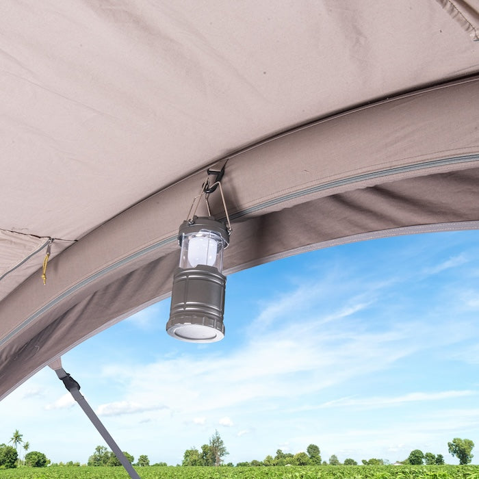 Innenansicht des BISALA 4 Familien Tunnelzelts von Tambu Outdoor mit aufgehängter grauer Campinglaterne und Blick auf grünes Feld und blauen Himmel