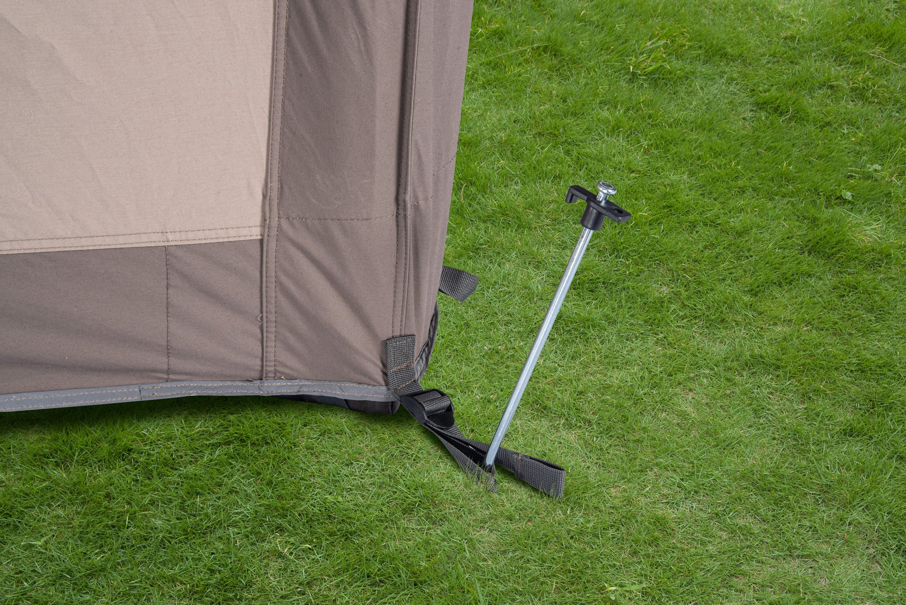 Ecke des BISALA 4 Familien Tunnelzelts von Tambu Outdoor mit einem Metallhering, der das Zelt am grünen Grasboden sichert