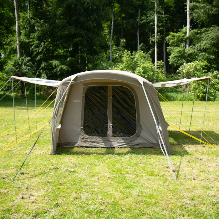 BISALA 4 Familien Tunnelzelt AIR von Tambu Outdoor, beige, für 4 Personen, mit großen Fenstern und zwei seitlichen Sonnensegeln auf einer grünen Wiese vor Wald