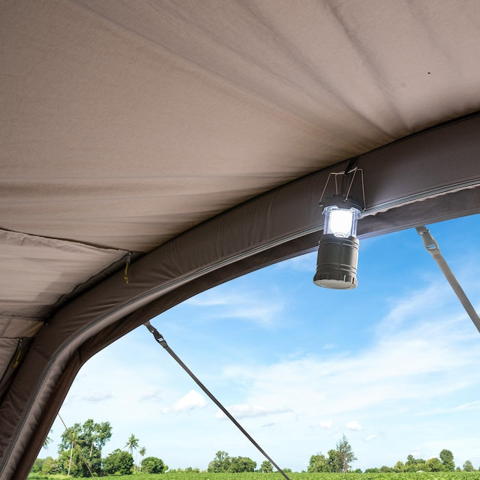 Innenansicht des BISALA 5 Familien Tunnelzelts von Tambu Outdoor mit aufgehängter Campinglampe und Blick auf grüne Landschaft und blauen Himmel
