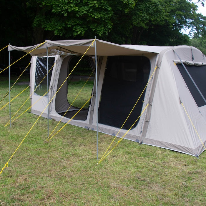 BISALA 5 Familien Tunnelzelt AIR von Tambu Outdoor in Beige mit großen Fenstern und Vordach auf grünem Gras vor Bäumen