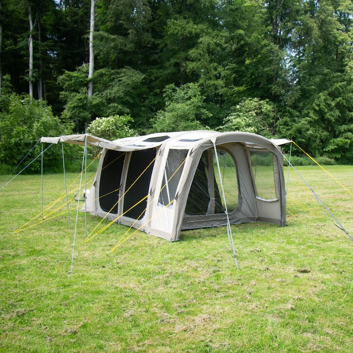 BISALA 4 Familien Tunnelzelt AIR von Tambu Outdoor, beige mit großen Fenstern und gelben Abspannleinen auf grüner Wiese vor Wald