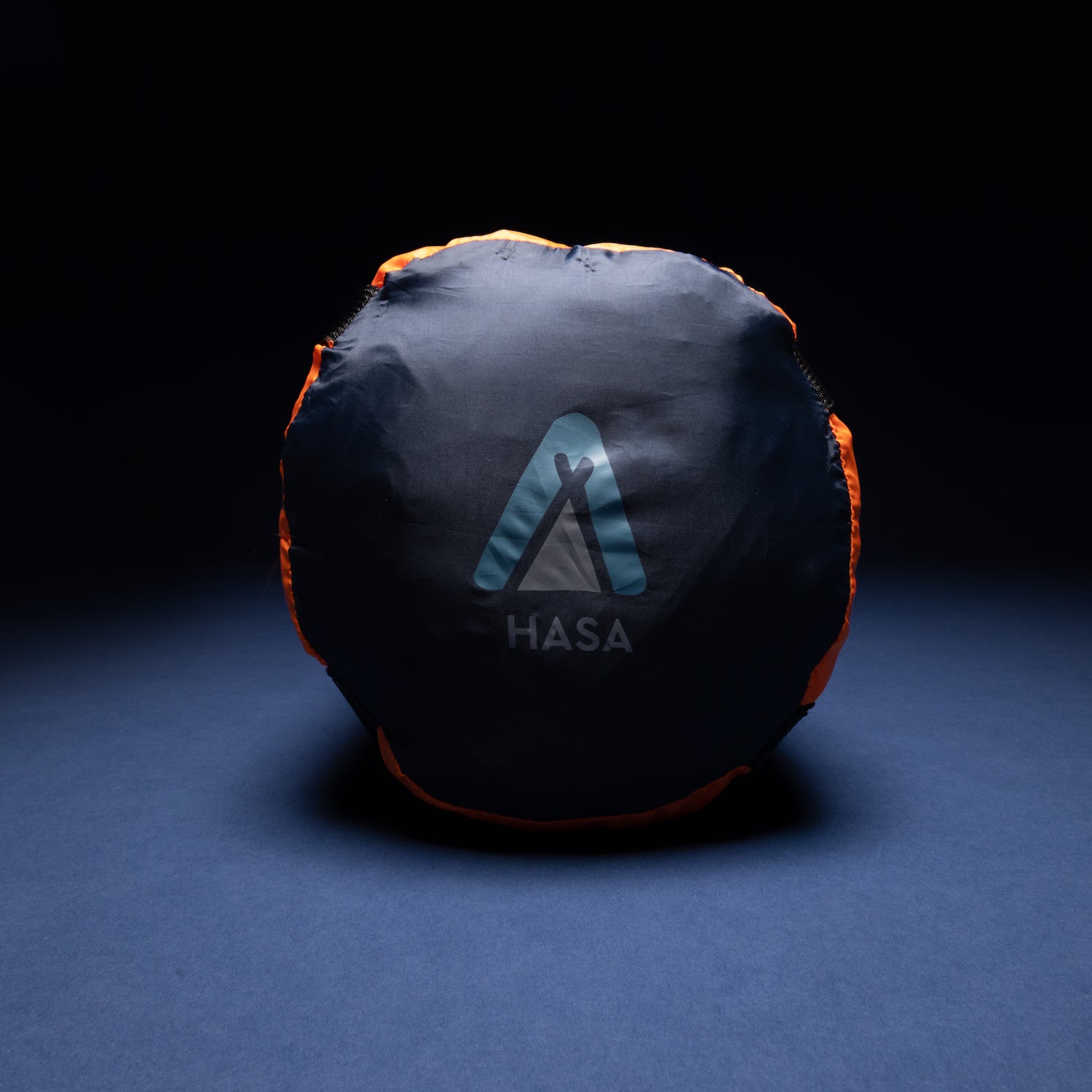 Runder, zusammengerollter Deckenschlafsack HASA 950 in schwarzer Hülle mit orangefarbenem Rand und Logo