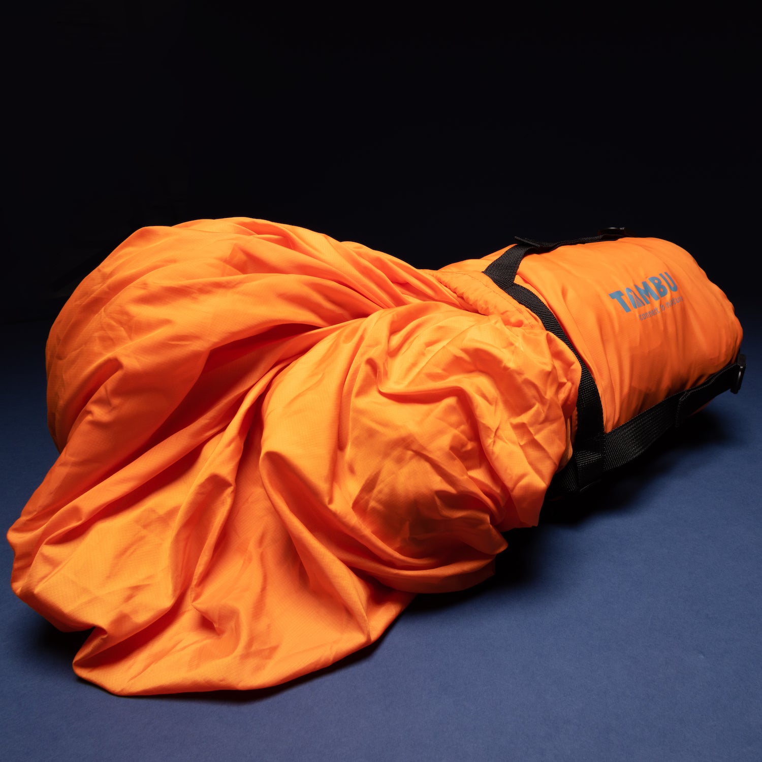 Oranger Deckenschlafsack HASA 950 von Tambu Outdoor halb zusammengerollt mit schwarzem Tragegurt auf dunklem Hintergrund