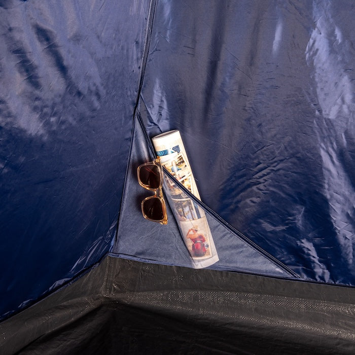 Innenansicht des blauen Innenzelts des HENA 4-Personen-Kuppelzelts von Tambu Outdoor mit einer kleinen Tasche, in der eine Sonnenbrille und eine zusammengerollte Zeitung liegen