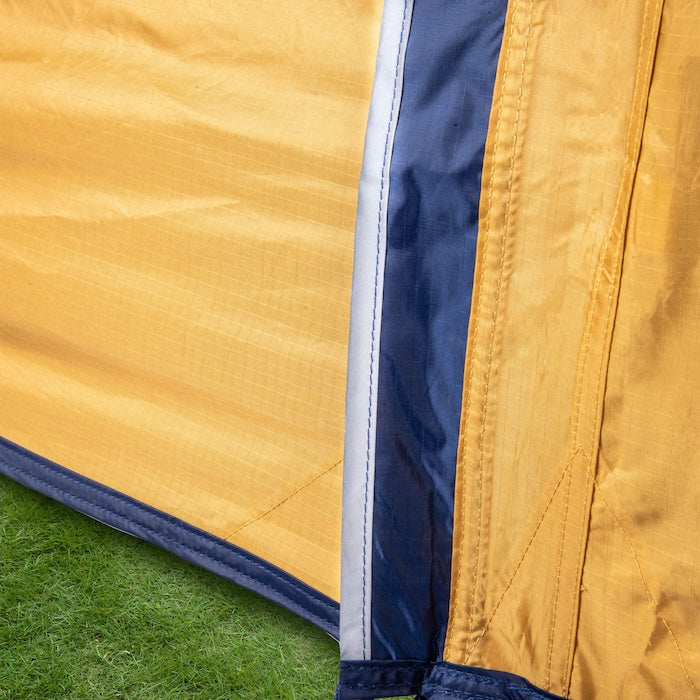 Nahaufnahme des gelb-blauen Stoffes und der Nähte des KUTIR 2.0 Leichtgewichts-Trekkingzelts von Tambu Outdoor auf grünem Gras