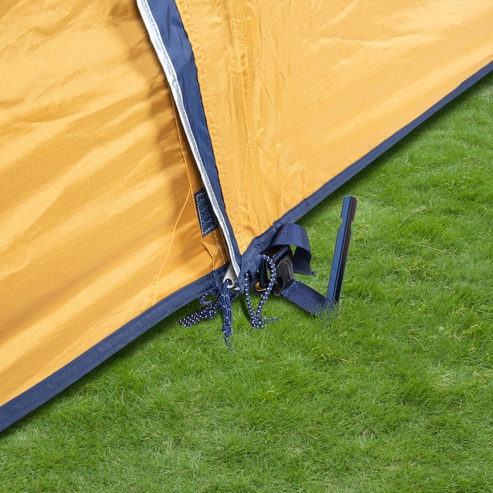 Nahaufnahme der Ecke des KUTIR 2.0 Leichtgewichts-Trekkingzelts von Tambu Outdoor in orange mit Reißverschluss und Befestigungsriemen auf grünem Gras