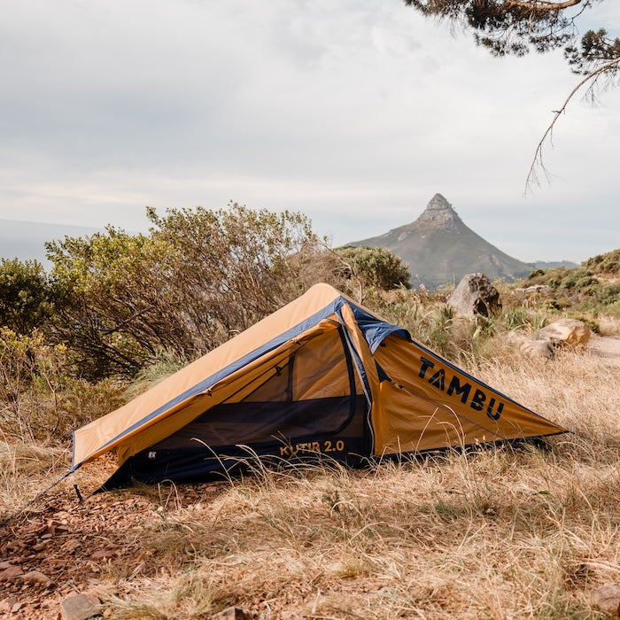 Leichtgewichts-Trekkingzelt KUTIR 2.0 von Tambu Outdoor in Gelb und Schwarz, auf trockenem Gras mit Berg im Hintergrund