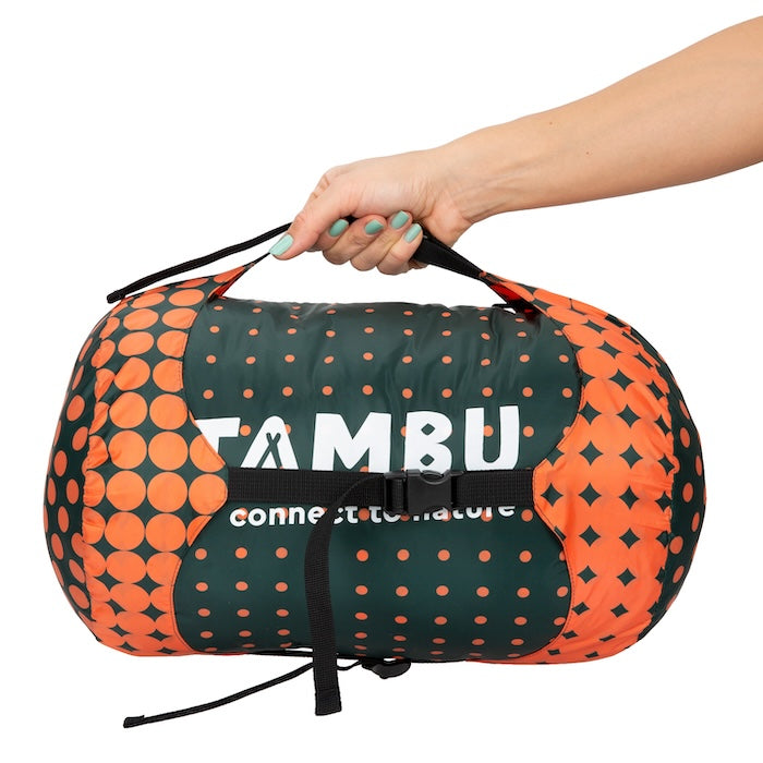 Hand hält den KARA Mumienschlafsack 1000 oder 1600 von Tambu Outdoor in grün-orange mit Tragegriff und Kompressionsriemen