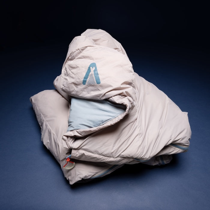 MOMI Mumienschlafsack 950 von Tambu Outdoor in hellgrauer Farbe mit Kapuze und blauem Innenfutter, liegend auf dunklem Untergrund