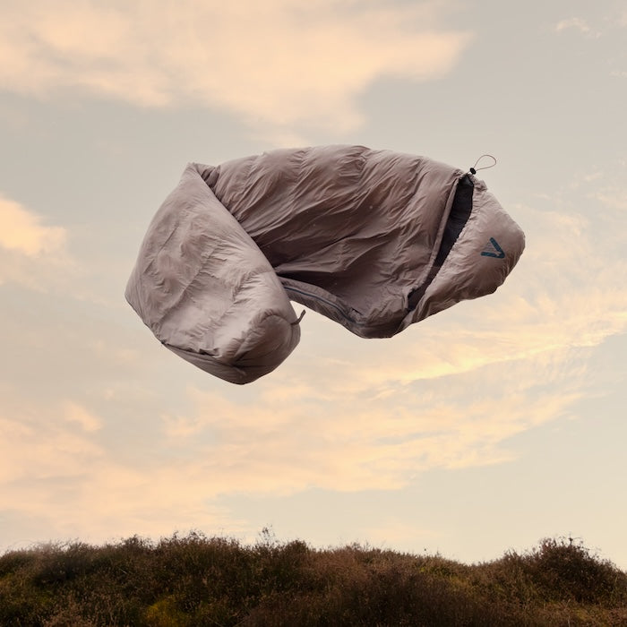 Grauer Mumienschlafsack MOMI 950 von Tambu Outdoor schwebt über einer Landschaft bei Sonnenuntergang