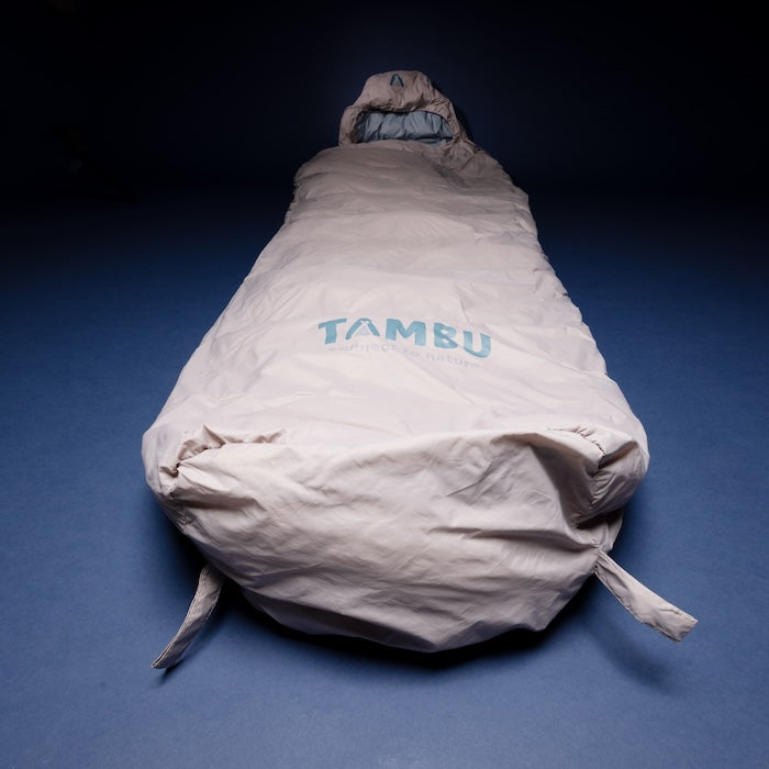 Grauer Mumienschlafsack MOMI 950 von Tambu Outdoor mit Kapuze und Zugbändern, flach liegend auf dunklem Untergrund