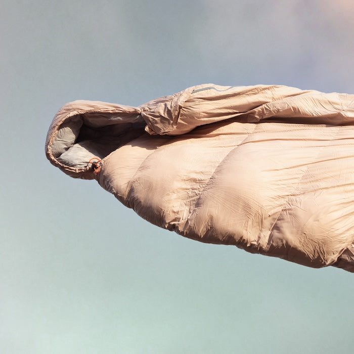 Grauer Mumienschlafsack MOMI 950 von Tambu Outdoor mit Kapuze, vor hellem Himmel schwebend