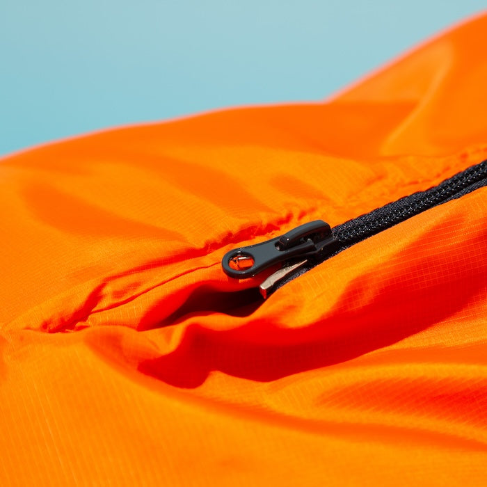 Nahaufnahme des schwarzen Reißverschlusses am orangefarbenen OFRA 800 Mumienschlafsack von Tambu Outdoor