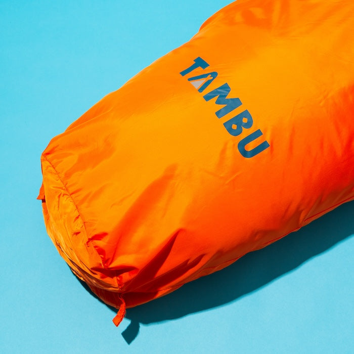 Orangefarbener OFRA 800 Mumienschlafsack von Tambu Outdoor auf blauem Hintergrund