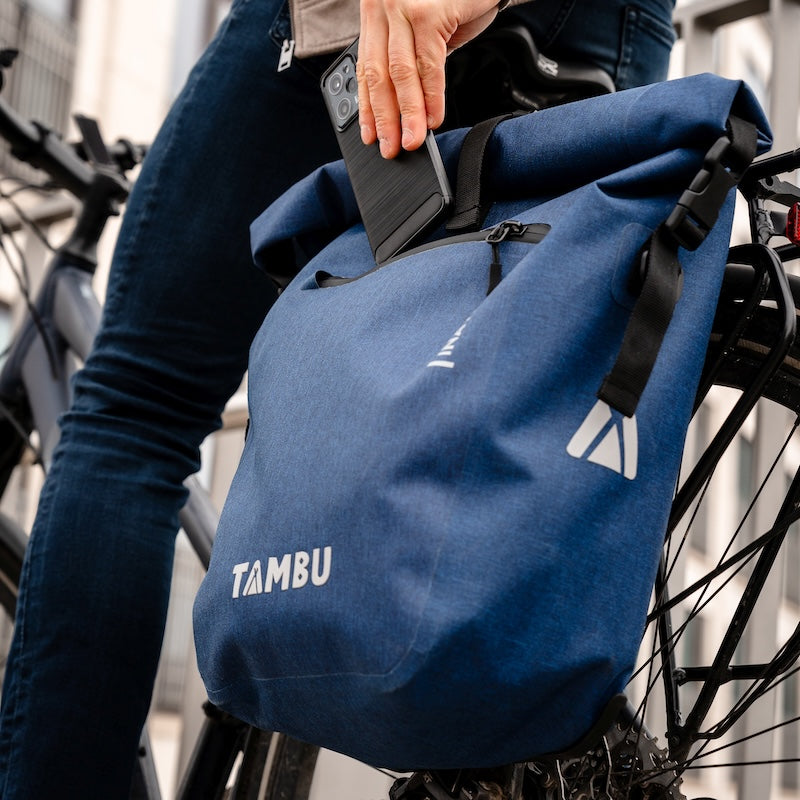 Blaue INAYA 20 Fahrradtasche von Tambu Outdoor, wasserabweisend, am Fahrrad befestigt, Person steckt Smartphone in die Tasche