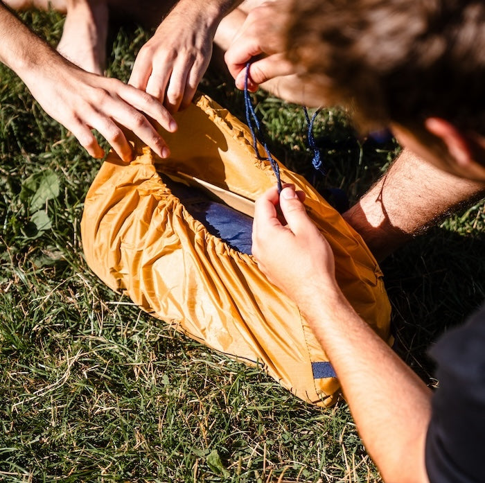Zwei Personen packen das gelbfarbene SURANGA 2.0 Leichtgewichts-Trekkingzelt von Tambu Outdoor auf Gras zusammen