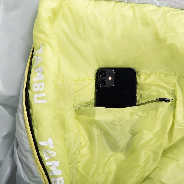 Gelber TONGI Mumienschlafsack 750 M  oder XL von Tambu Outdoor mit Reißverschlusstasche, in der ein schwarzes Smartphone steckt