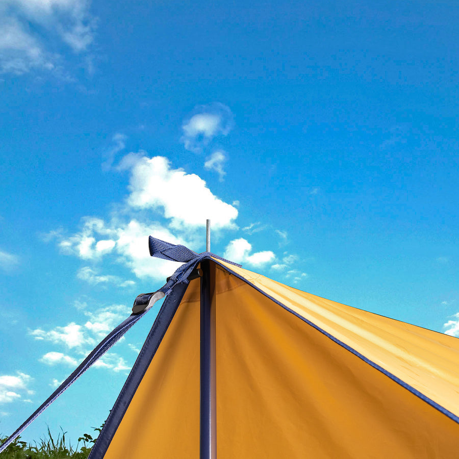 Gelbes multifunktionales Sonnensegel CHADA von Tambu Outdoor, gespannt mit blauem Band und Metallstange unter blauem Himmel mit Wolken