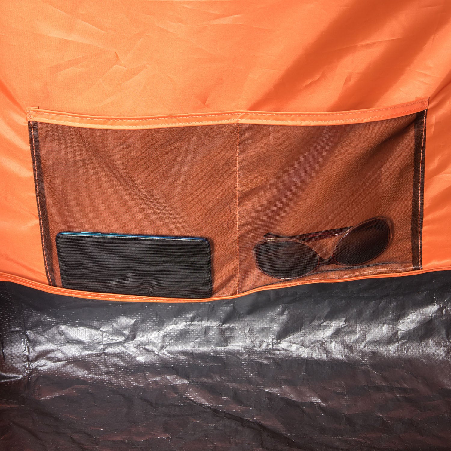 Innenansicht des orangefarbenen Familienzelts Mandapa 4 von Tambu Outdoor mit zwei Stofftaschen, eine enthält ein Smartphone, die andere eine Sonnenbrille