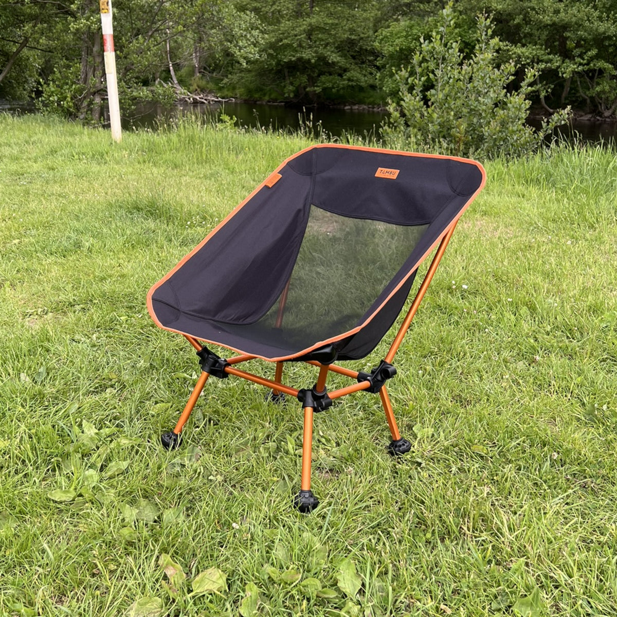 Leichter Campingstuhl BATASA von Tambu Outdoor in Schwarz mit orangefarbenem Rahmen, zwei Sitzhöhen, auf Gras im Freien
