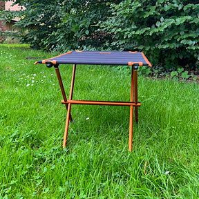 Leichter Campingtisch BATISTA von Tambu Outdoor mit schwarzer Tischplatte und orangefarbenem Aluminiumgestell auf grünem Gras