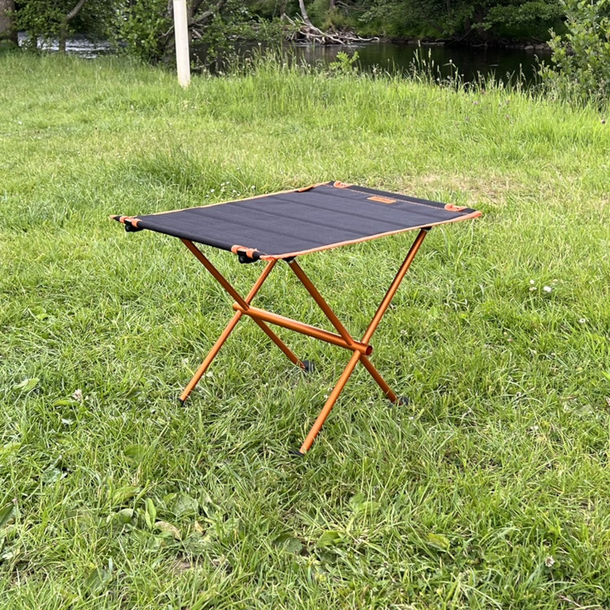 Leichter Campingtisch BATISTA von Tambu Outdoor mit schwarzer Aluminiumplatte und orangefarbenem Gestell auf Wiese